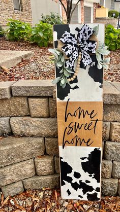 a sign that says home sweet home in front of a brick wall with leaves on it