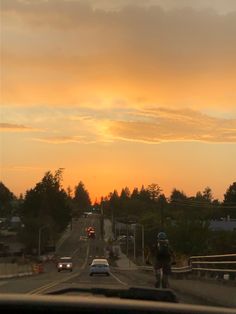 the sun is setting over a street with cars driving down it and people walking on the sidewalk