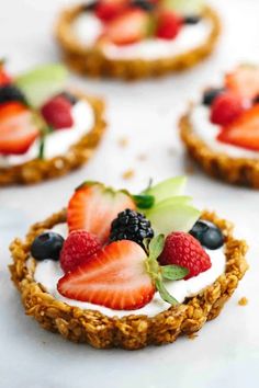 small desserts with strawberries, blueberries and kiwi on top are sitting on a white surface