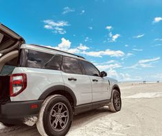 the back end of a white suv with its trunk open on a sandy beach under a blue sky