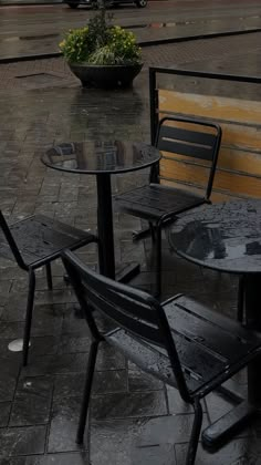 two black tables and chairs sitting on a wet sidewalk