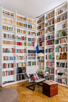 a living room filled with lots of books on white bookcases next to a wooden floor