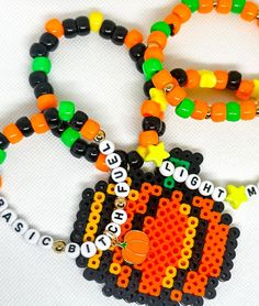 three beaded necklaces with beads and letters on them, one has an orange pumpkin