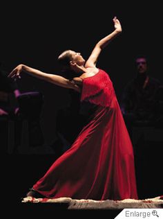 a woman in a red dress dancing on stage with her arms stretched out to the side