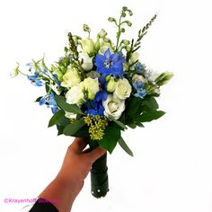 a hand holding a bouquet of white and blue flowers on top of green stems with greenery