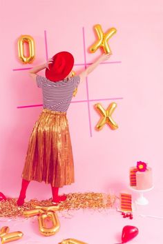 a woman wearing a red hat standing in front of a pink wall with gold letters