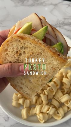 a hand holding a sandwich over pasta on a plate with the words turkey pesto sandwich