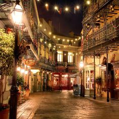 an empty city street at night with lights strung from the buildings and balconies