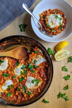 a skillet filled with food next to a bowl of lemons and parsley