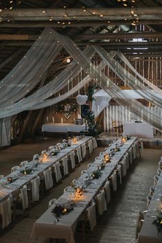 an indoor wedding venue with tables and chairs covered in white cloths, decorated with lights