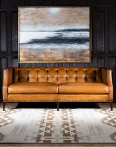 a brown leather couch sitting in front of a painting