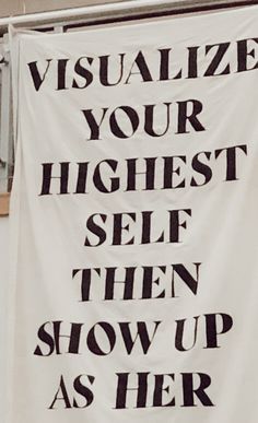 a white banner hanging from the side of a building that says visualize your highest self then show up as her