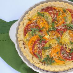 a pizza with tomatoes, cheese and herbs in a pie pan on a green napkin