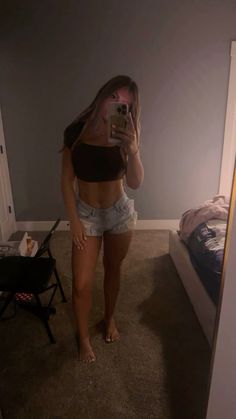 a woman taking a selfie in her bedroom while wearing denim shorts and a crop top