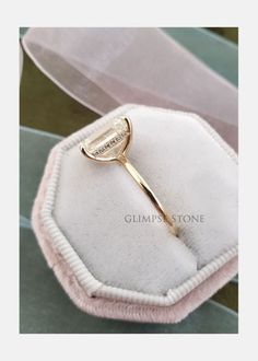 a close up of a gold ring on a white velvet box with a pink ribbon around it