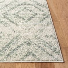 a white rug with green and gray designs on the top is laying on a wooden floor