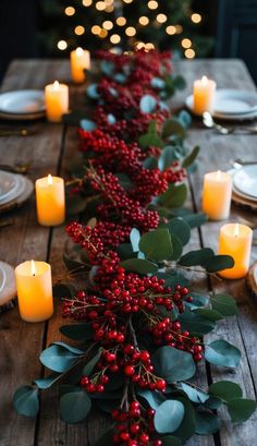 the table is set with candles, greenery and red berries for a festive look