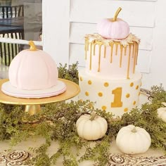 three tiered cake decorated with white pumpkins and greenery on a table in front of a door