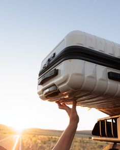 a person holding up a piece of luggage in the back of a truck at sunset