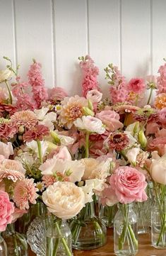 a bunch of vases filled with pink and white flowers on a wooden table next to a wall