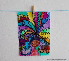 a colorful painting hanging on a clothes line next to a white wall and blue string