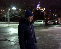 a woman standing in the middle of an empty parking lot at night with snow falling all around her