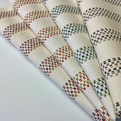 four pieces of white fabric with multicolored squares on the top one is folded in half