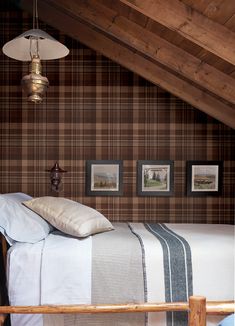 a bed sitting under a wooden ceiling next to two pictures on the wall above it