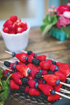 strawberries and blueberries are on skewers with toothpicks in them