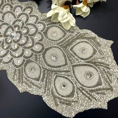 an intricately designed table cloth with white flowers on the side and black surface behind it