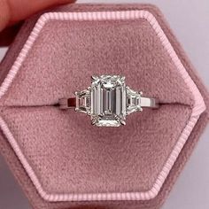 an emerald cut diamond ring in a pink velvet box with the band around it's edge