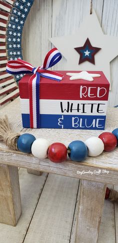 a red, white and blue box with beads on a bench in front of an american flag wreath