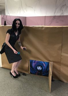 a woman standing next to a cardboard box with a painting on it