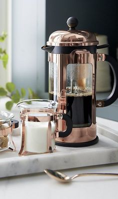 a coffee maker sitting on top of a counter next to a glass container and spoon