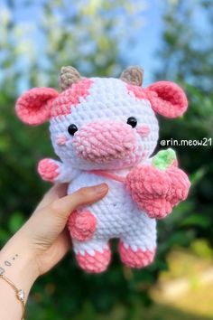 a hand holding a pink and white crocheted cow