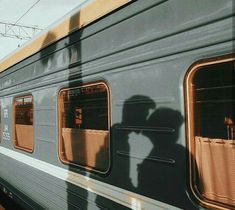 the shadow of two people on the side of a passenger train as it passes by