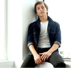 a young man sitting on top of a toilet in front of a window with his eyes closed