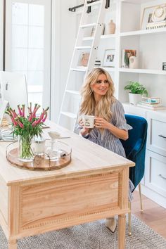 a woman sitting at a desk with a cup in her hand and flowers on the table