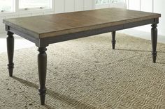 a large wooden table sitting on top of a carpeted floor next to two windows