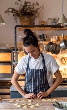 a woman standing in front of a cutting board with food on it and cooking utensils hanging from the ceiling