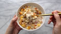 two hands holding a white bowl filled with oatmeal and fruit