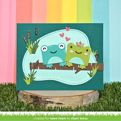 a card with two frogs sitting on a tree branch in front of a rainbow colored background