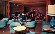 a group of people sitting around tables in a room with blue chairs and lamps on the walls