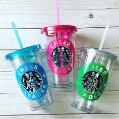 three starbucks cups with lids and straws in different colors on a white wooden surface