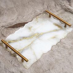 a white marble tray with gold handles on a furry surface next to a business card holder