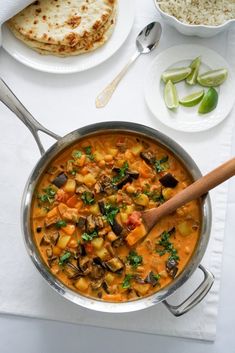 a stew with vegetables and meat in a pan on a table next to some pita bread