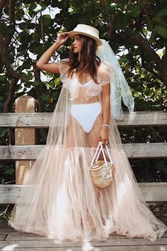 a woman in a white bikinisuit and hat standing on a wooden deck wearing a veil