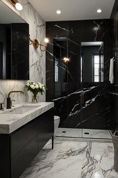 a black and white bathroom with marble counter tops, gold fixtures and lights on the wall