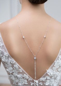 the back of a woman's dress wearing a long necklace with flowers on it