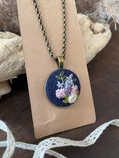 This hand embroidered pendant features a delicate floral design. The perfect accessory for you, or a great gift idea for a loved one. A beautiful and unique conversation piece. Each piece is unique. The design is set in an antique gold pendant and comes with a chain. Note that this is a handmade item. Actual colors may vary. Due to light and screen display the colours might be shown slightly different. *PLEASE NOTE* ITEM DETAILS - pendant measures 1" x1"  - chain secured with a lobster clasp,  - Bohemian Jewelry With Floral Embroidery For Gifts, Bohemian Embroidered Necklace For Gift, Artisan Embroidered Jewelry For Gift, Embroidered Pendant Necklace For Gift, Antique Gold Pendant, Hand Embroidered Pendant, Jewelry Embroidery, Hand Embroidered Jewelry, Embroidered Pendant